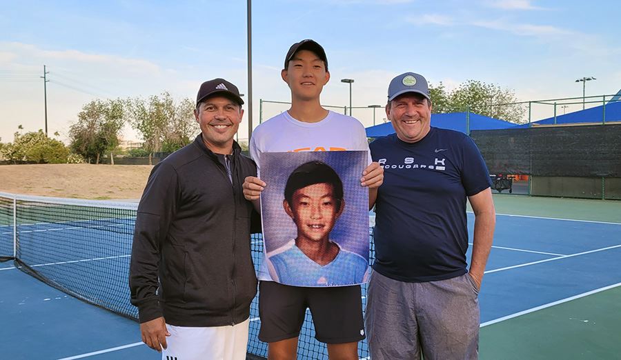  Adam Sun poses on tennis court with his coaches while holding a large photo of himself from grade s